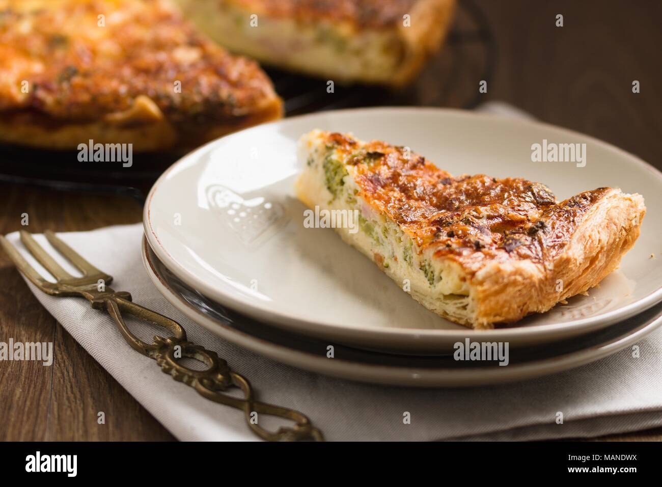 A forma di triangolo pezzo di torta di verdure o quiche, servita su un piatto ornato di forcella di ottone Foto Stock