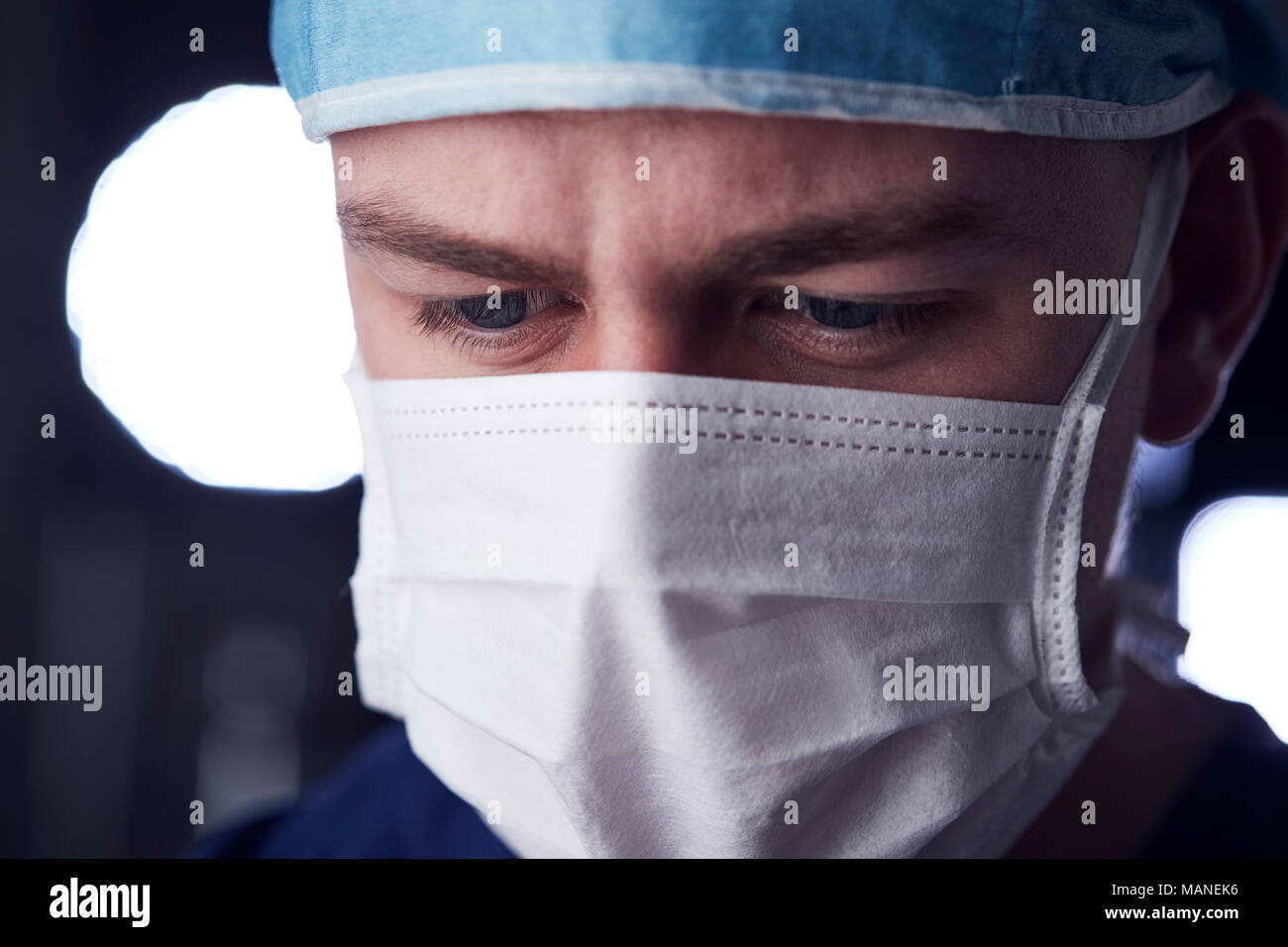 Maschio lavoratore del settore sanitario in scrubs, colpo alla testa, guardando verso il basso Foto Stock