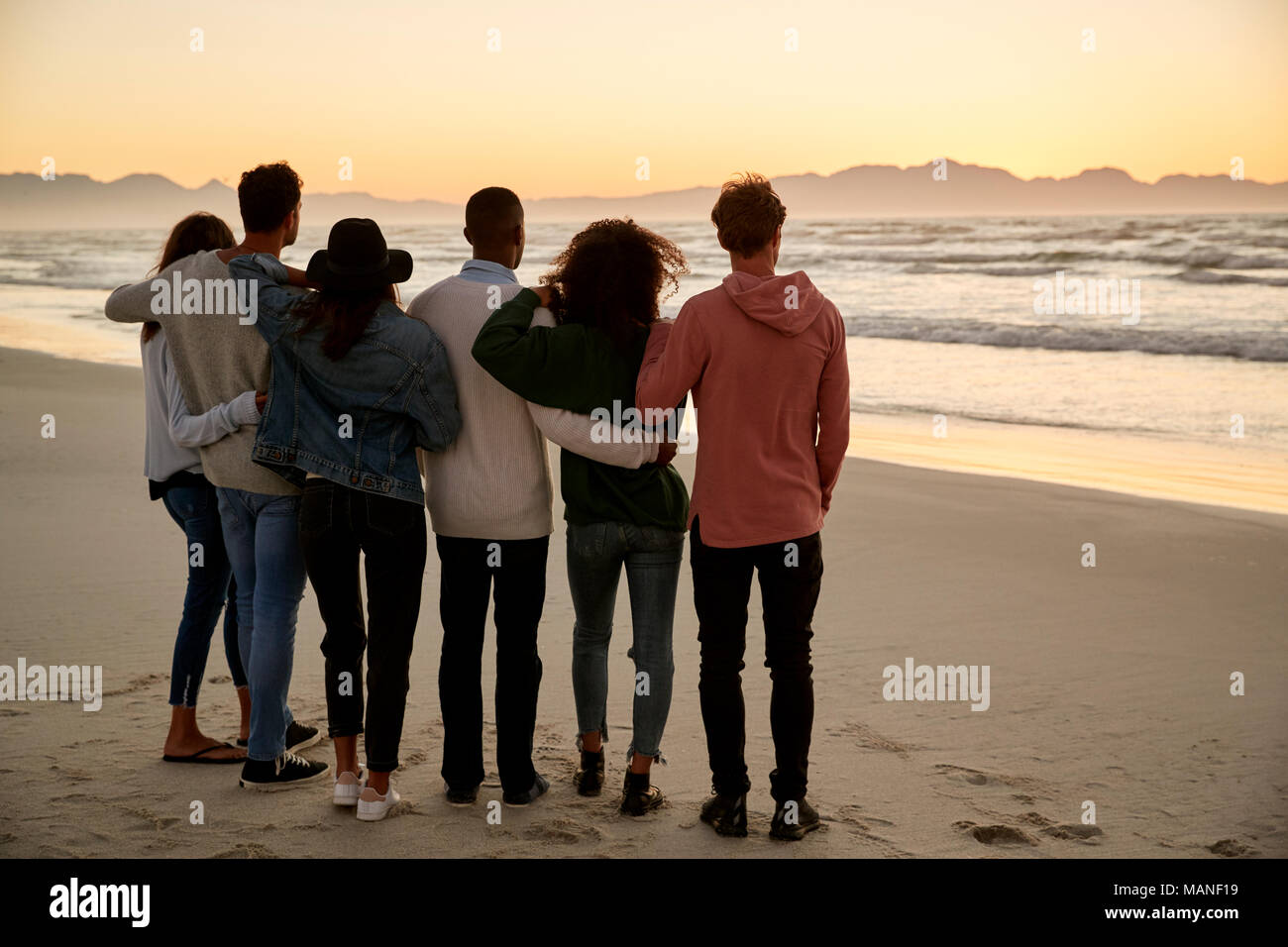 Gruppo di amici sulla Spiaggia Invernale la visione di insieme di Sunrise Foto Stock