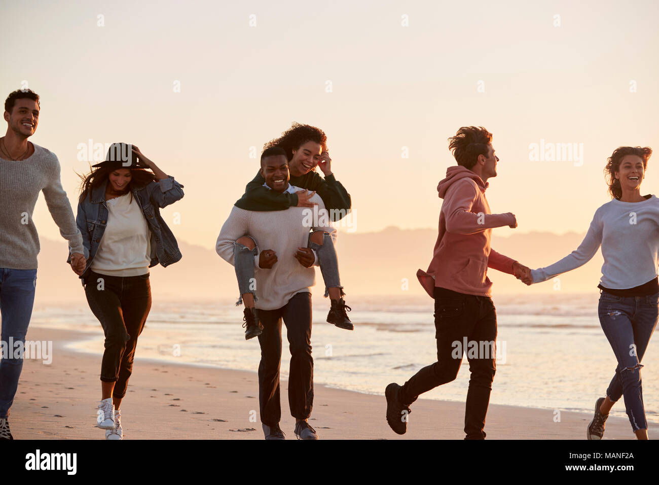 Gruppo di amici divertendosi in esecuzione lungo la spiaggia invernale insieme Foto Stock