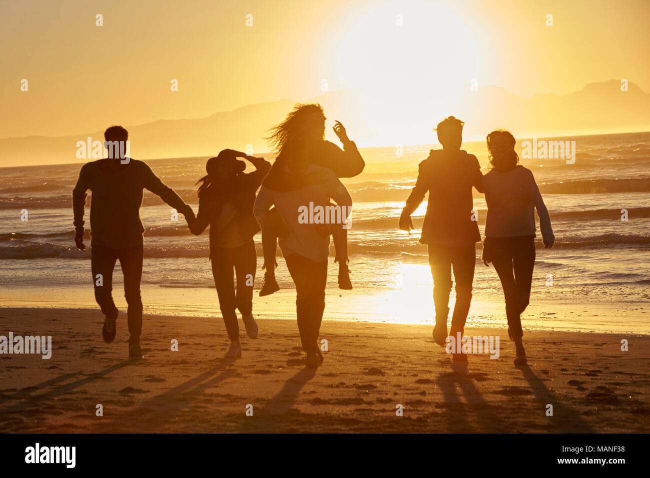 Silhouette di amici divertendosi in esecuzione lungo la Spiaggia Invernale Foto Stock