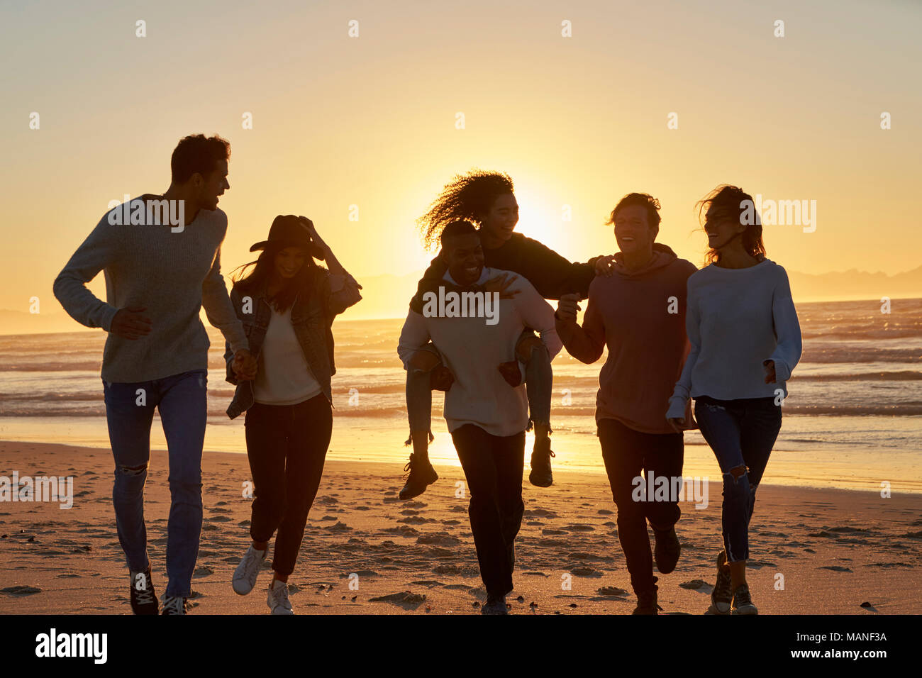 Silhouette di amici divertendosi in esecuzione lungo la Spiaggia Invernale Foto Stock