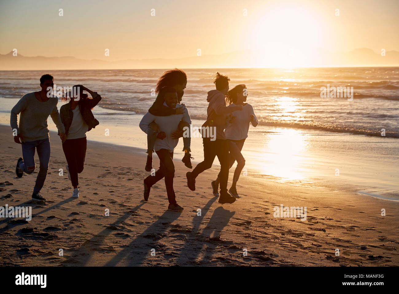 Silhouette di amici divertendosi in esecuzione lungo la Spiaggia Invernale Foto Stock