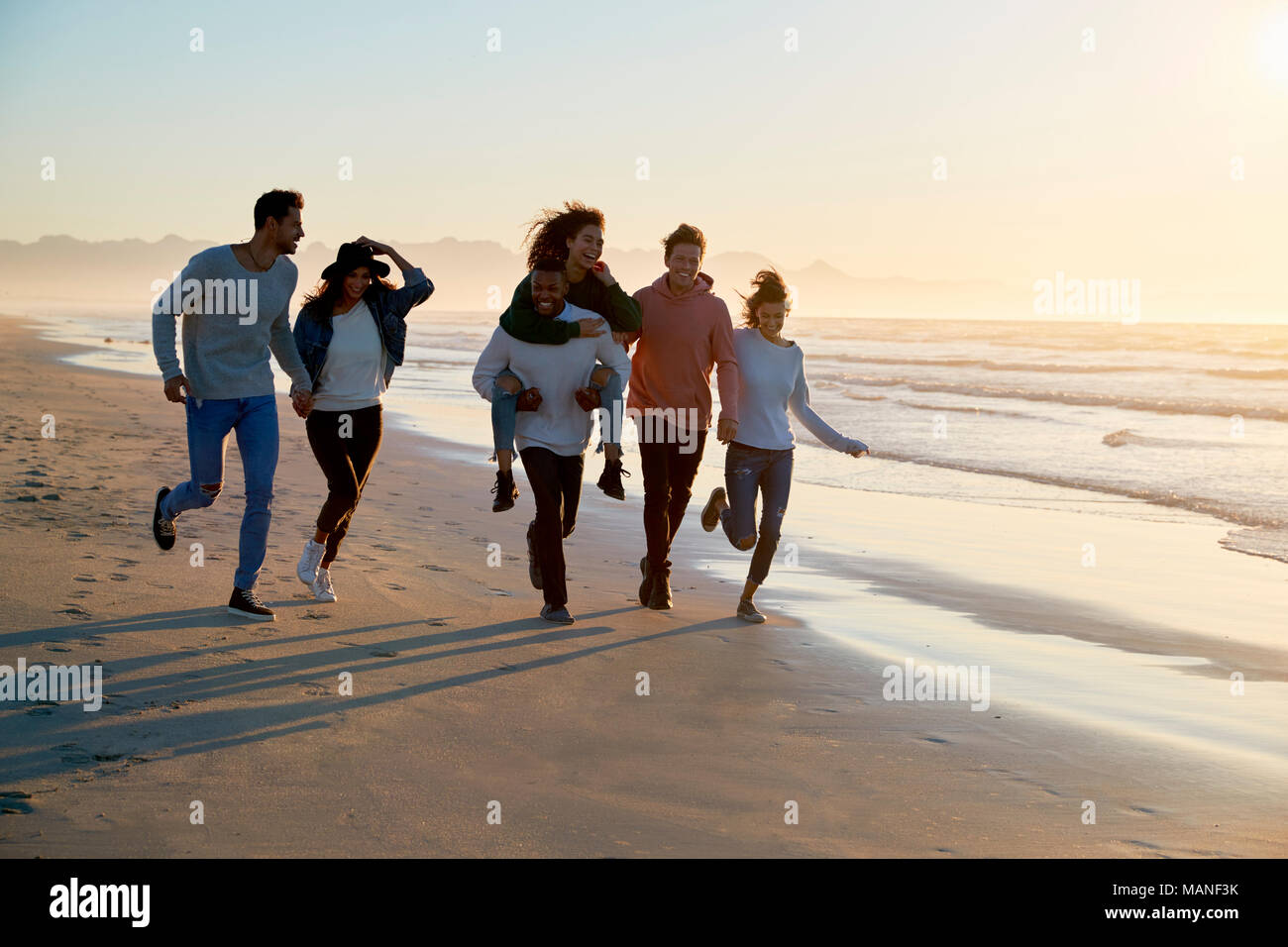 Gruppo di amici divertendosi in esecuzione lungo la spiaggia invernale insieme Foto Stock