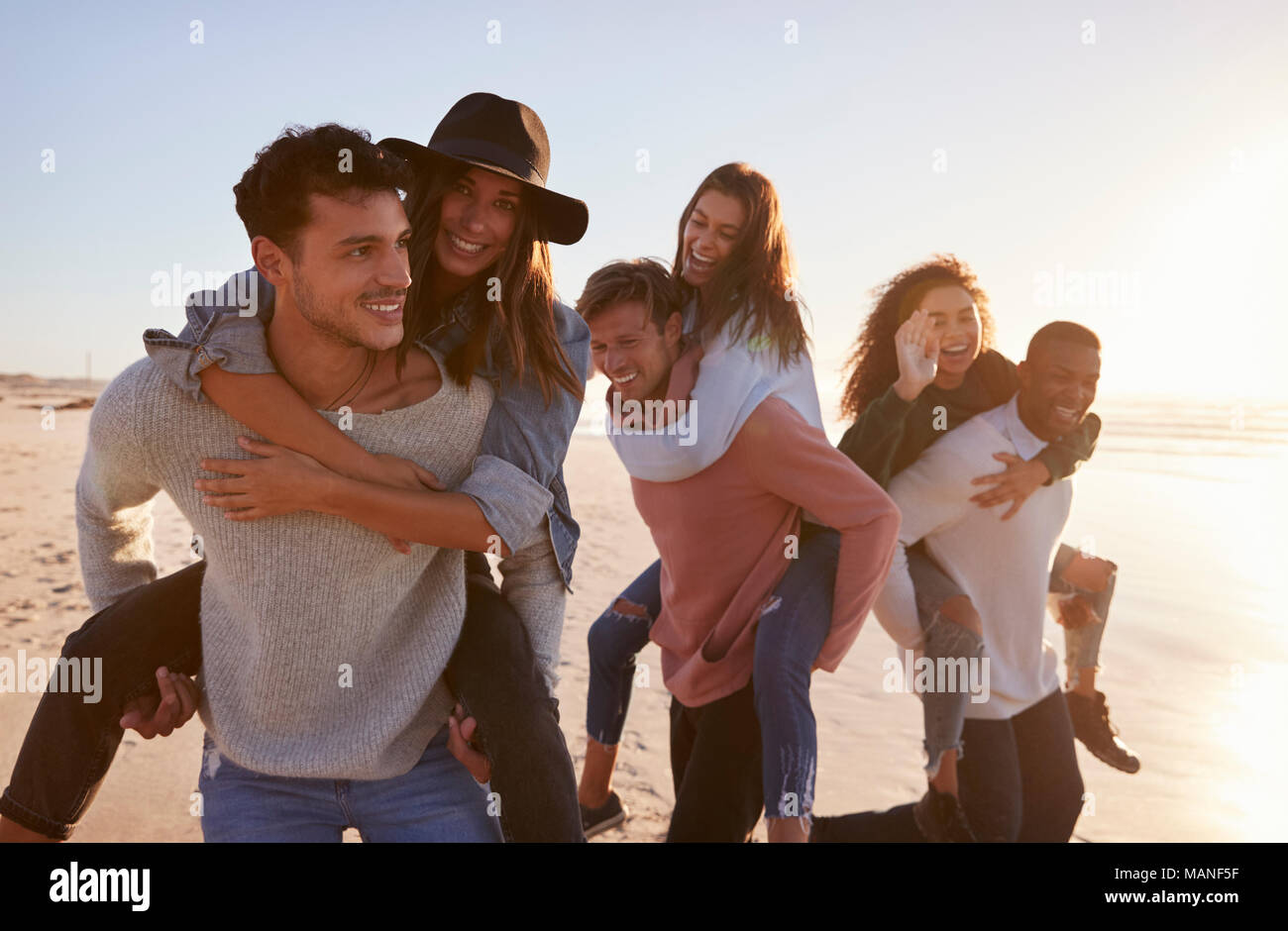 Gruppo di amici avente Piggyback gara sulla Spiaggia Invernale insieme Foto Stock