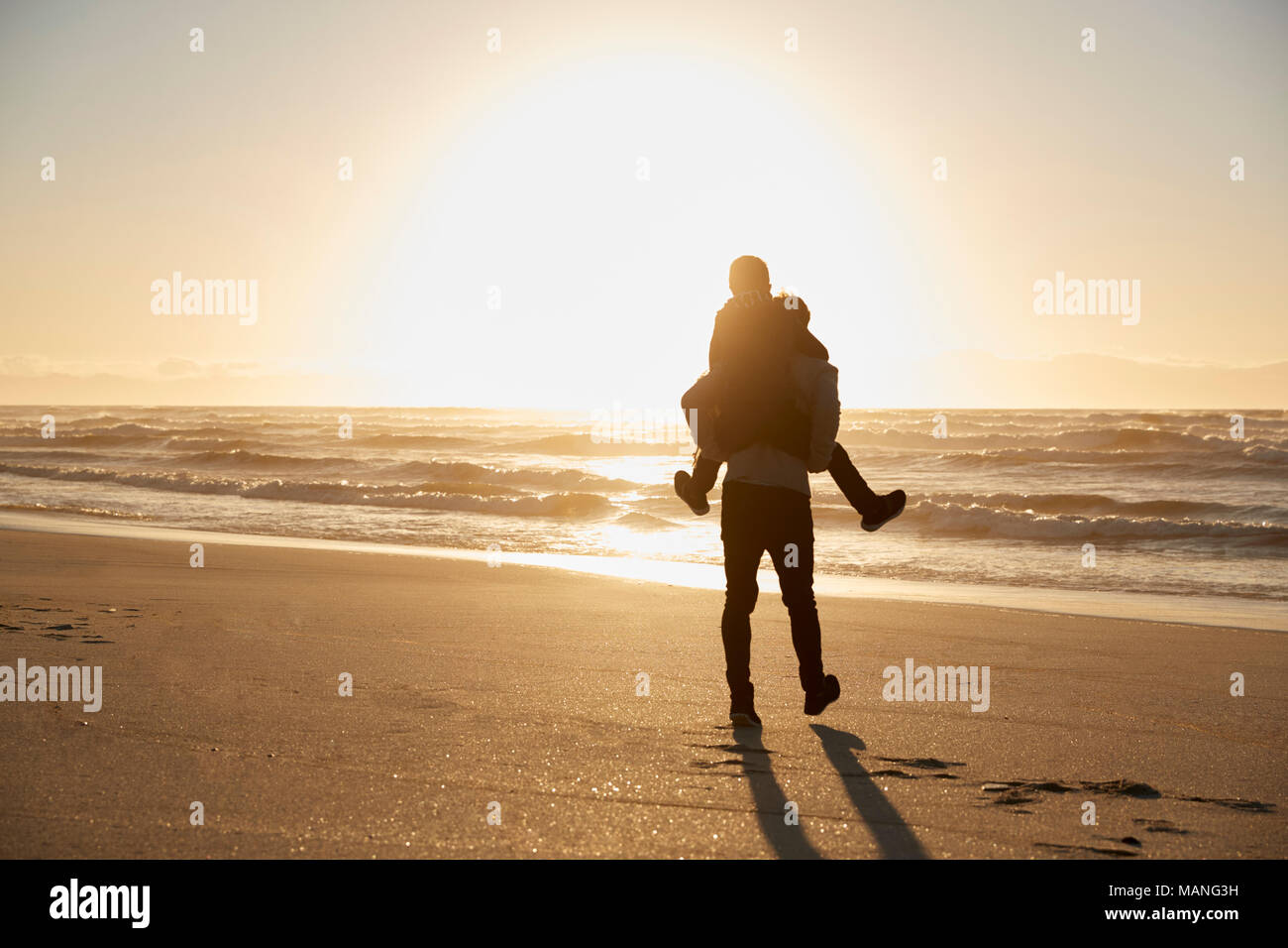 Silhouette di padre dando figlio piggyback sulla Spiaggia Invernale Foto Stock