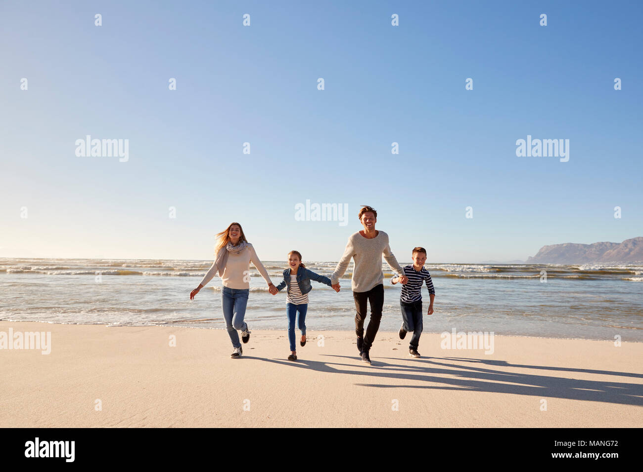 Famiglia sulla Spiaggia Invernale tenendo le mani e correre verso la telecamera Foto Stock