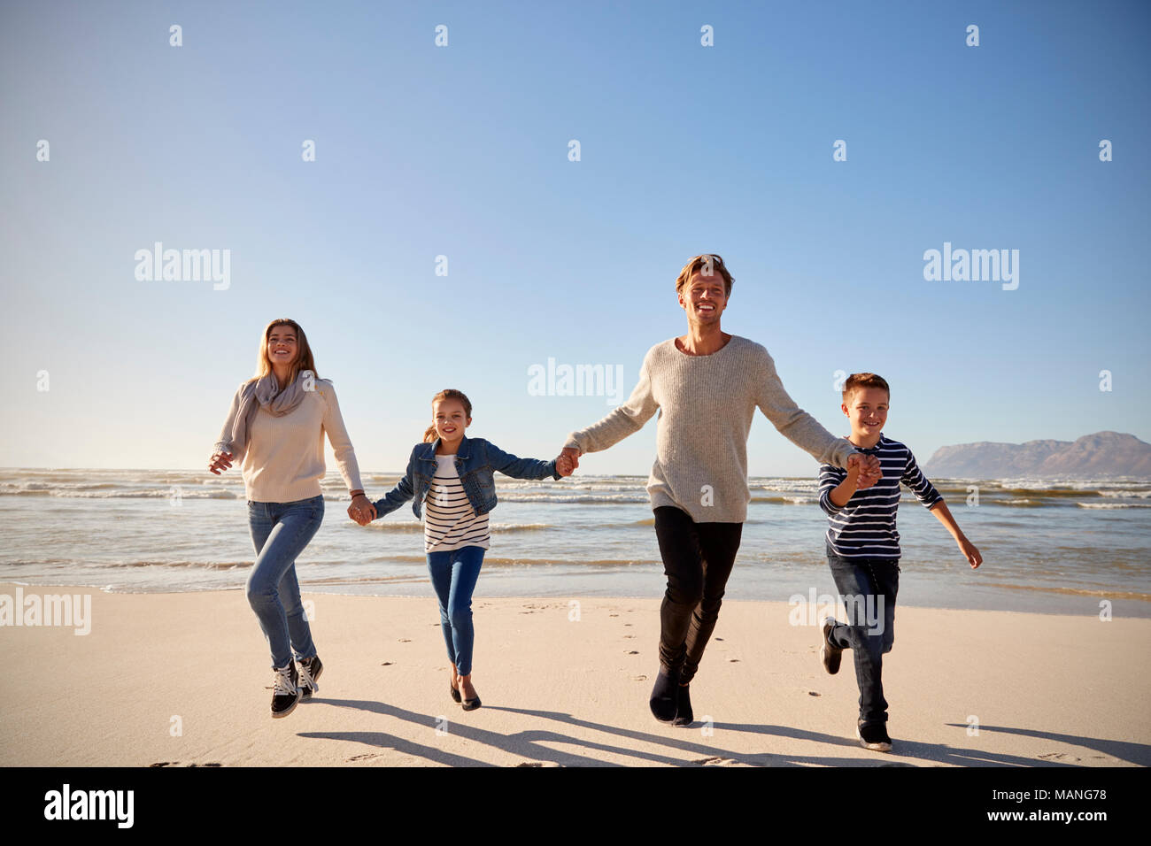 Famiglia sulla Spiaggia Invernale tenendo le mani e correre verso la telecamera Foto Stock