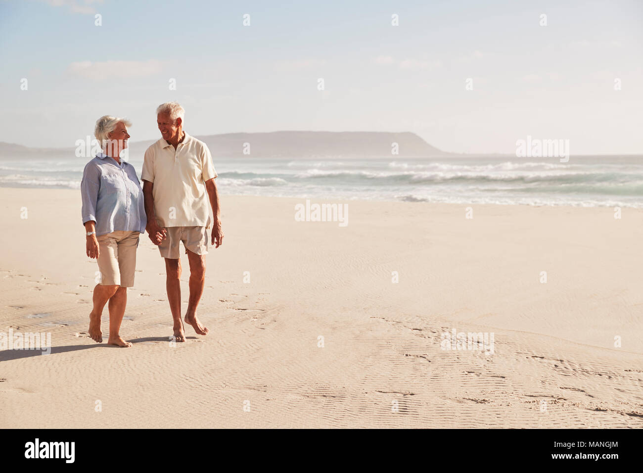 Senior pensionati giovane camminando lungo la spiaggia mano nella mano insieme Foto Stock