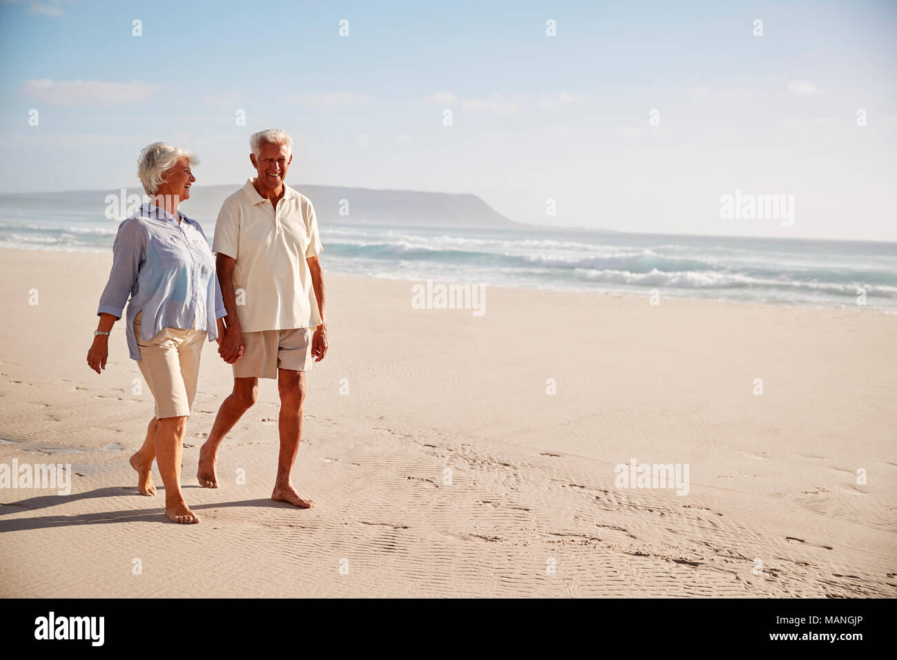 Senior pensionati giovane camminando lungo la spiaggia mano nella mano insieme Foto Stock
