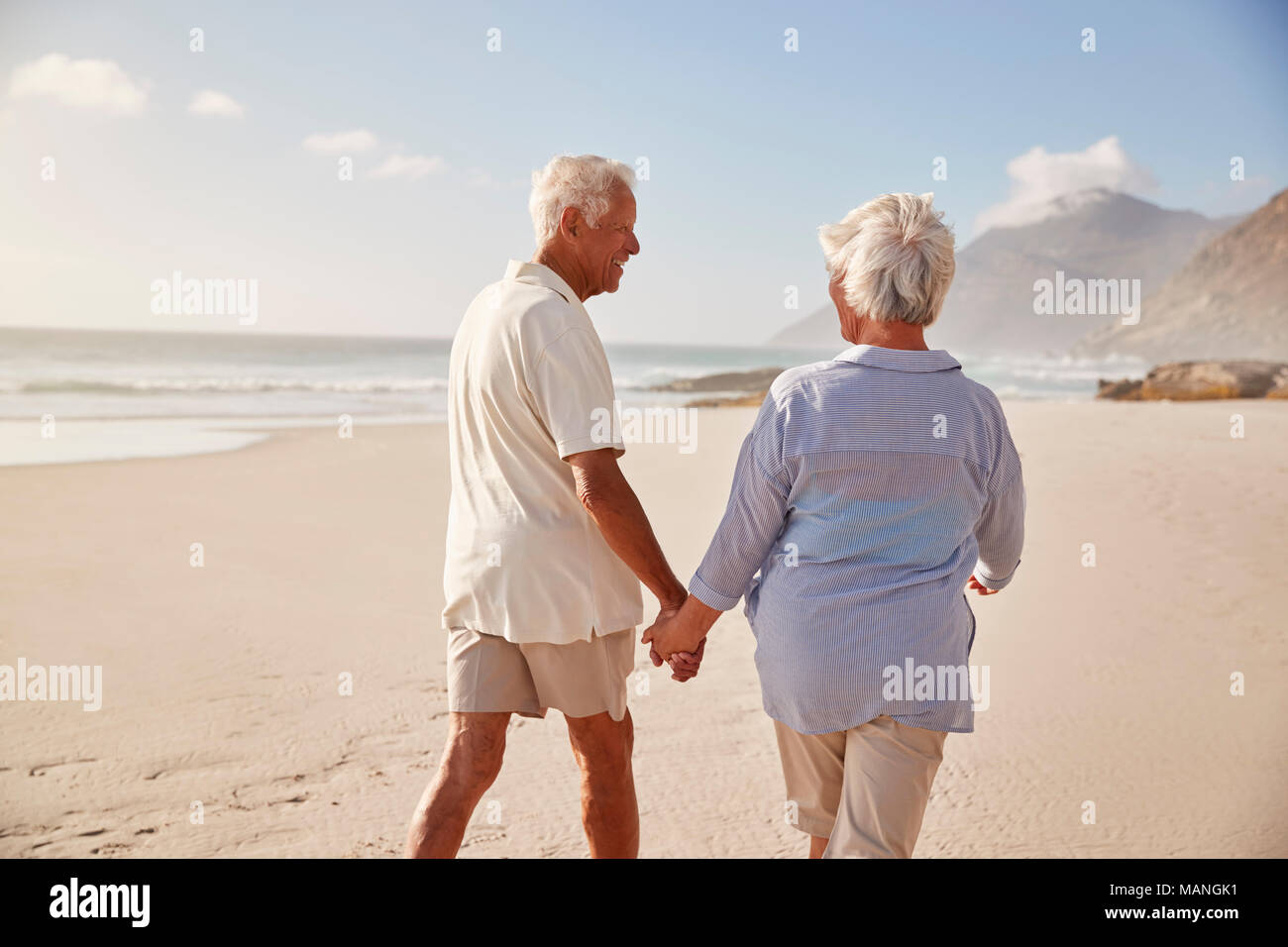 Vista posteriore della coppia Senior camminando lungo la spiaggia mano nella mano Foto Stock