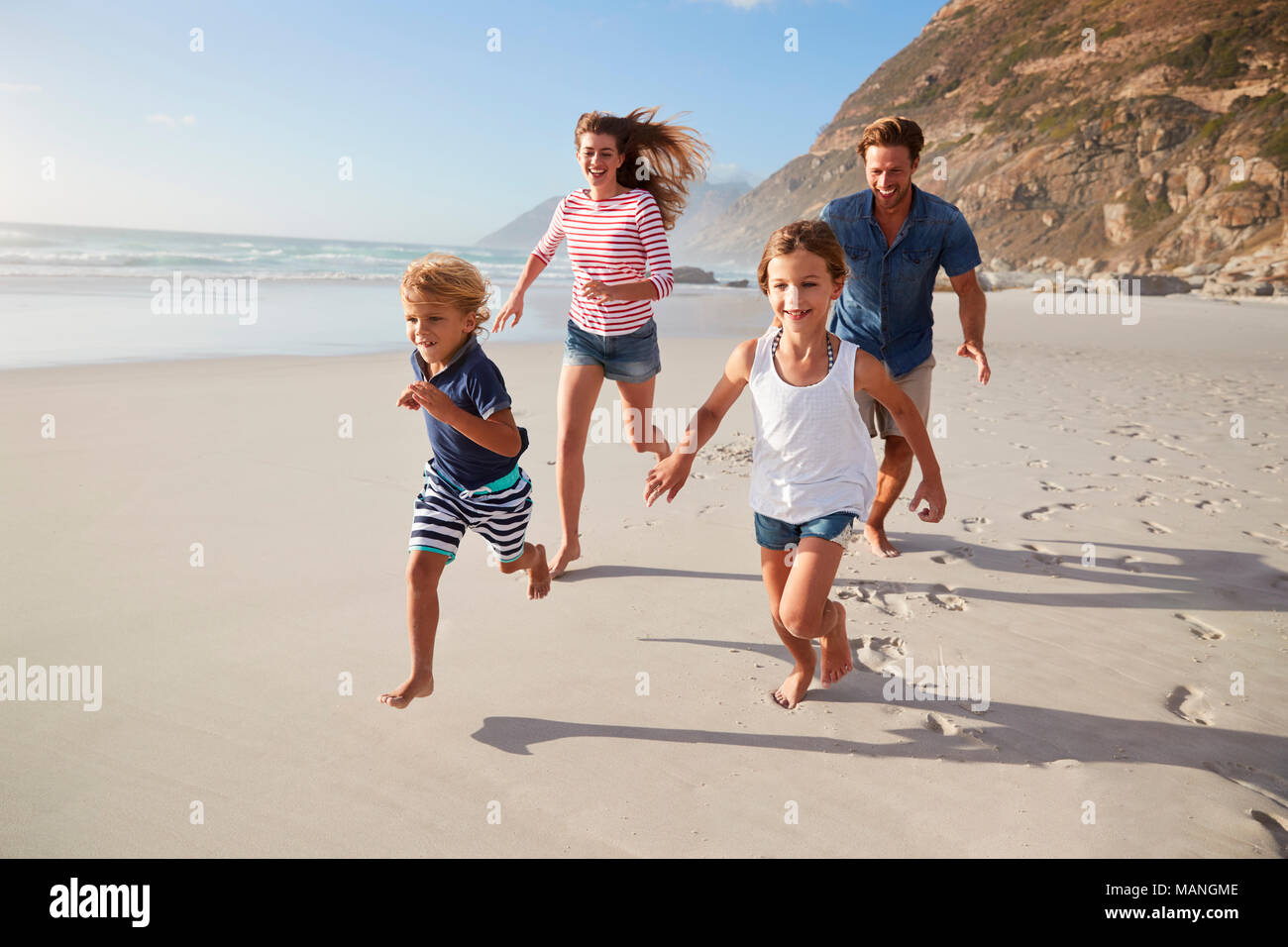 I genitori che corre lungo la spiaggia con i bambini in vacanza estiva Foto Stock