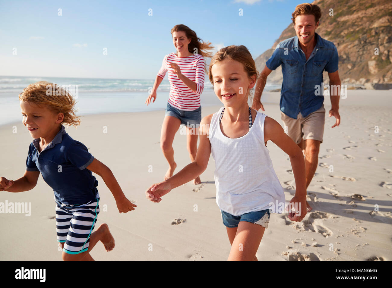 I genitori che corre lungo la spiaggia con i bambini in vacanza estiva Foto Stock