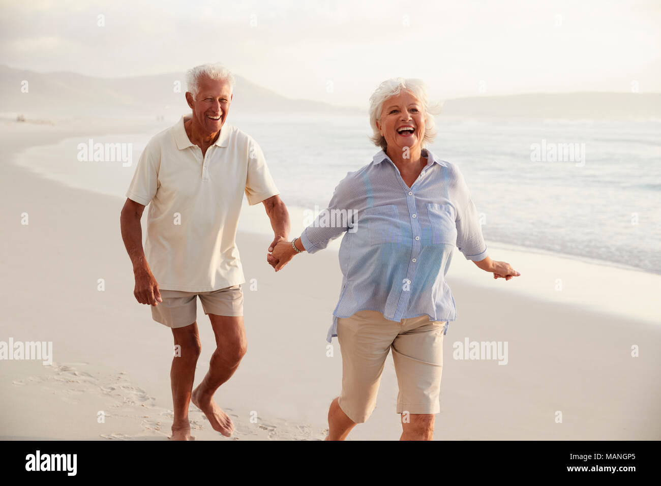 Senior pensionati giovane che corre lungo la spiaggia mano nella mano insieme Foto Stock