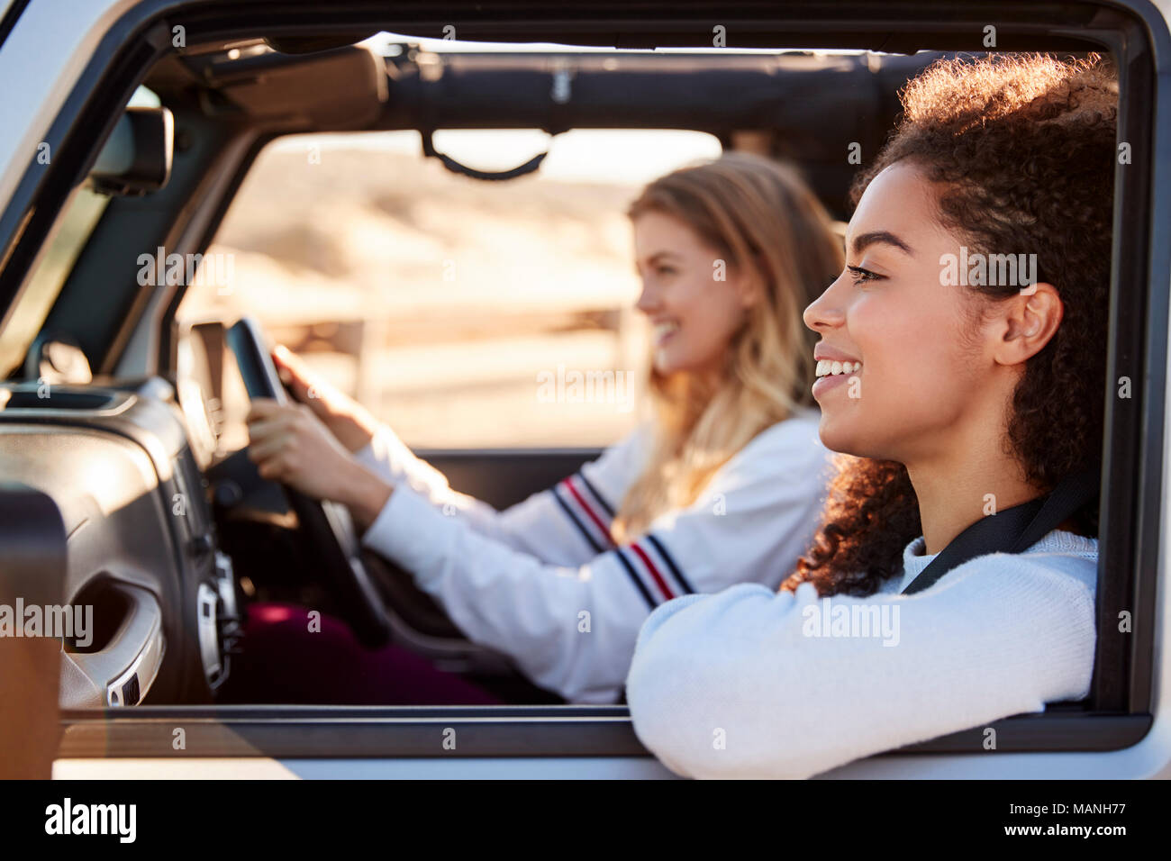 Due giovani amici di sesso femminile alla guida di una vettura al sole, vista laterale Foto Stock