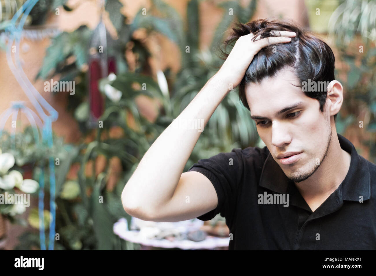 Ritratto di un giovane uomo all'esterno con la mano sul suo pelo guardando verso il basso, di pensare e di grave. Foto Stock