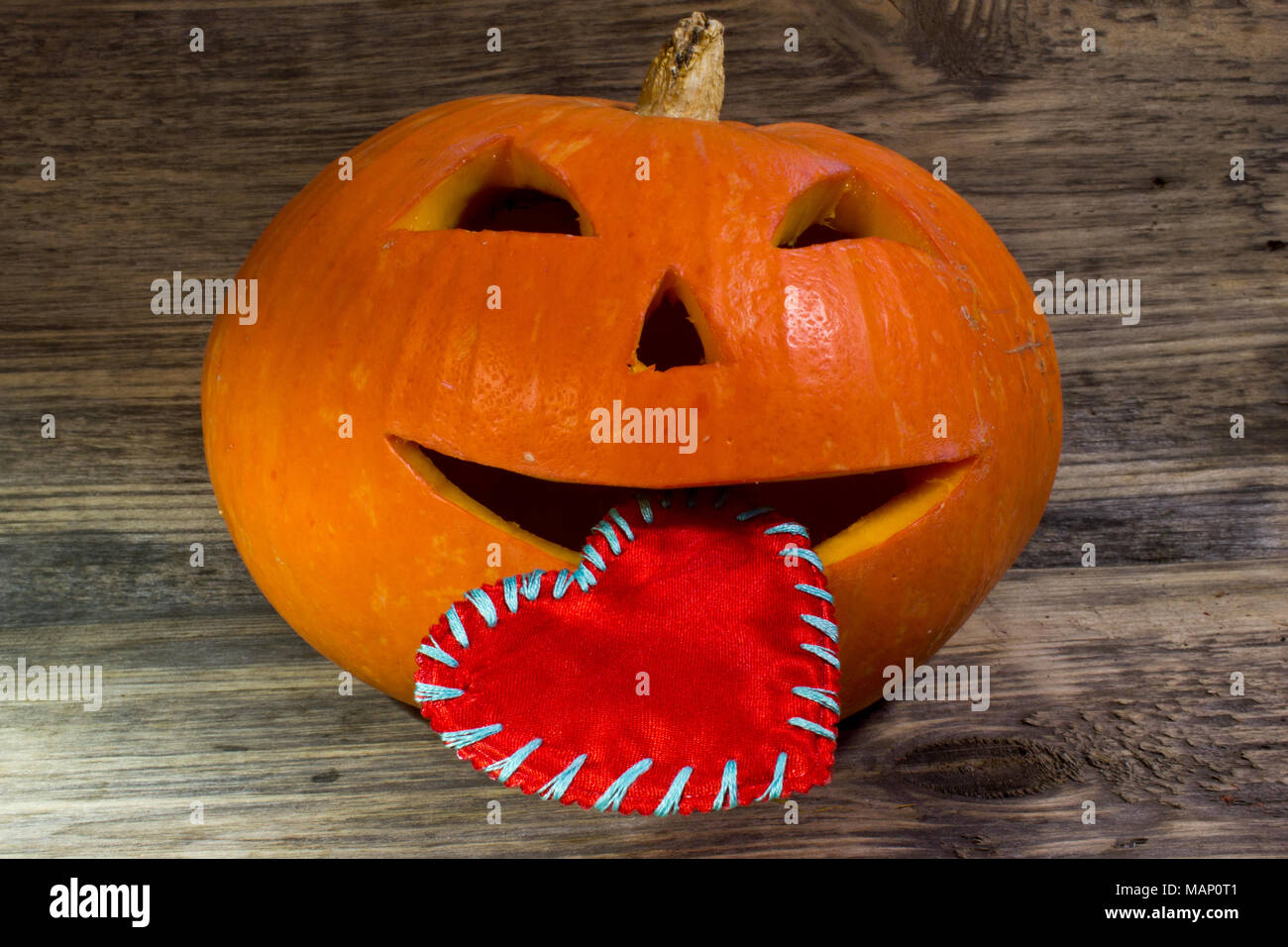 Zucca di Halloween è holding nella sua bocca un cuore rosso per il giorno di San Valentino su sfondo di legno Foto Stock