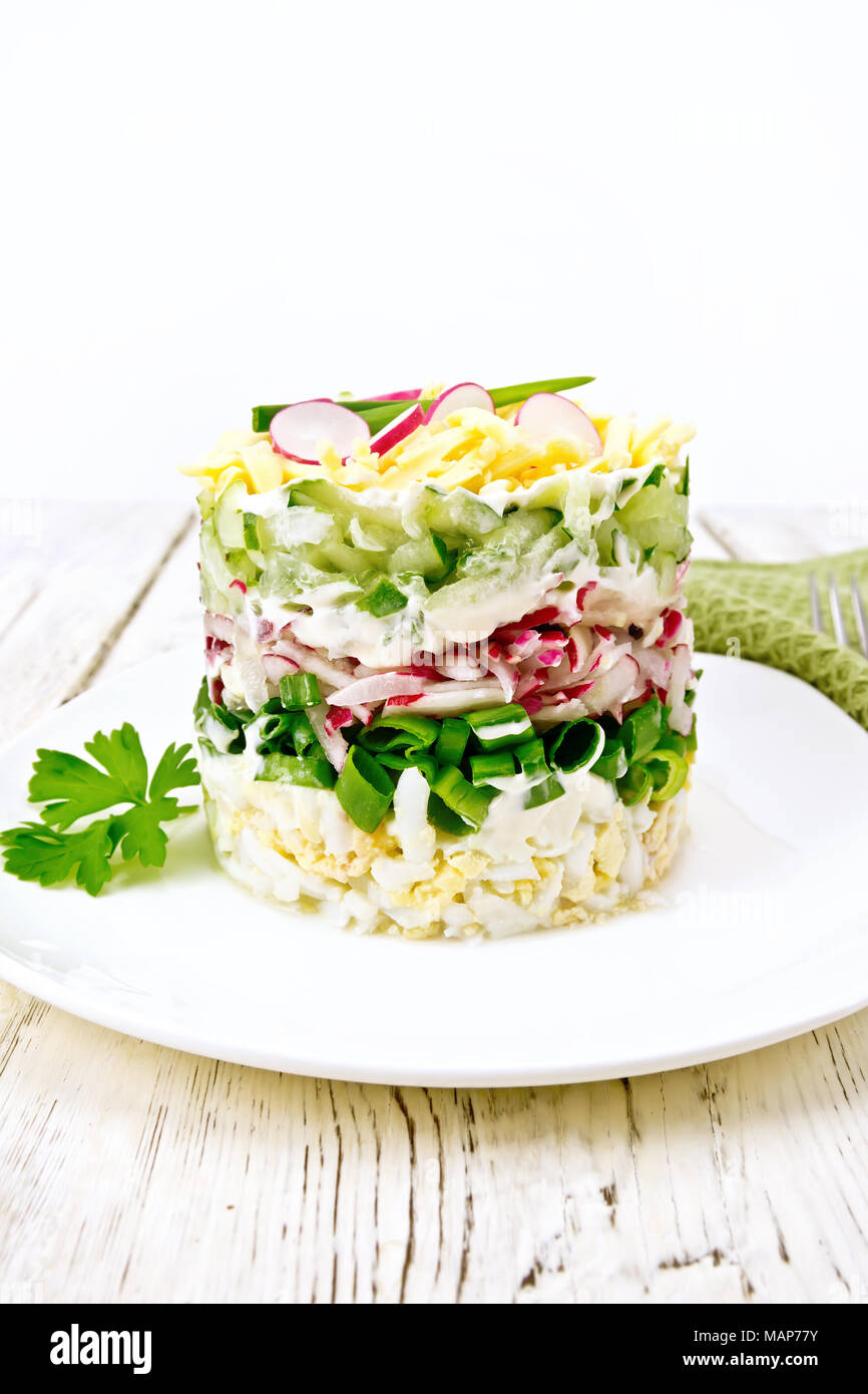 Insalata stratificato con un ravanello, cetriolo, uova, i cipollotti e il formaggio in piastra, tovagliolo sulla tavola di legno sfondo Foto Stock