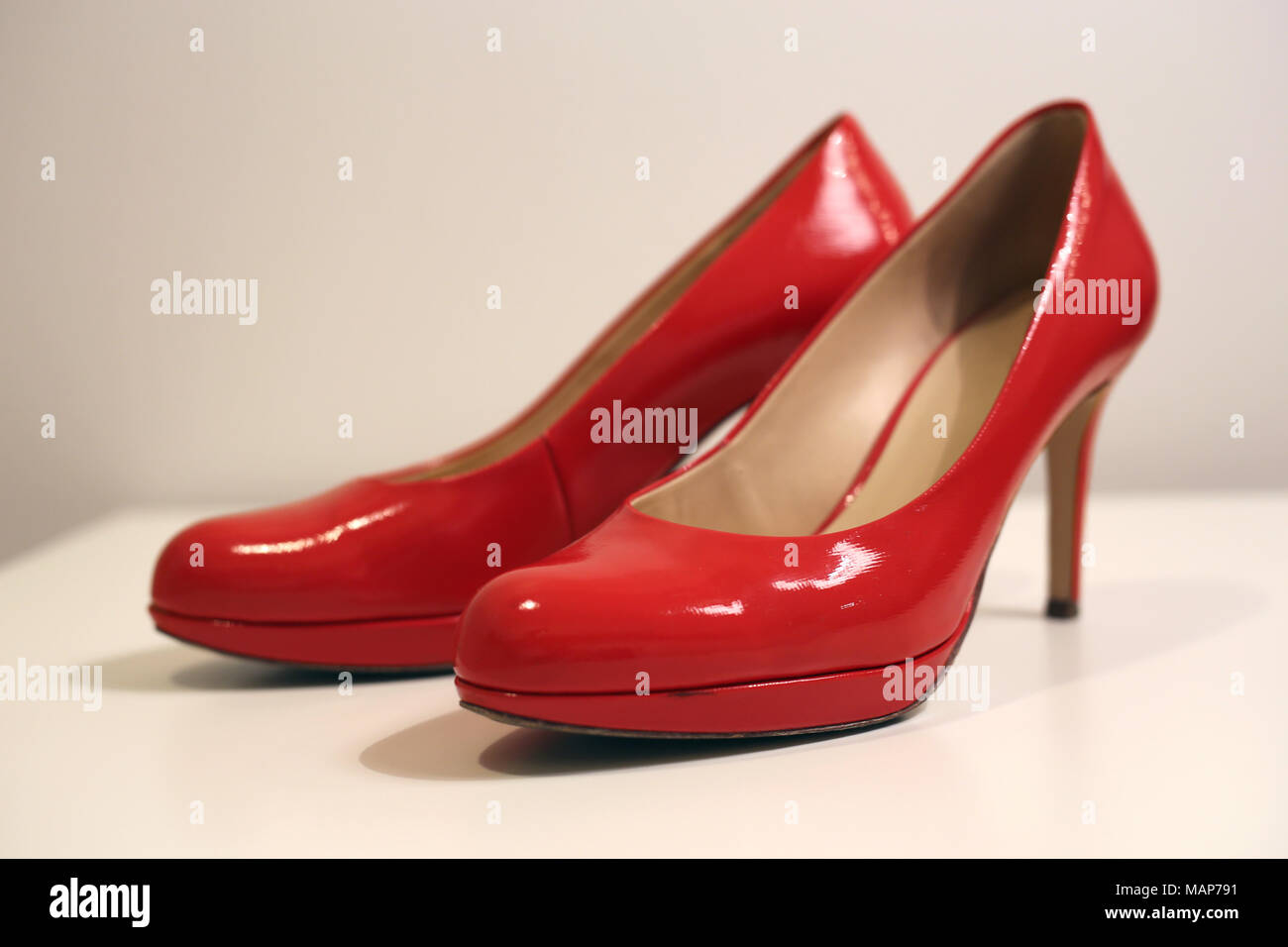 Un stil la vita di un paio di tacchi alti su un tavolo bianco. Le scarpe sono di colore rosso in pelle lucida scarpe e lo sfondo è bianco. Foto Stock