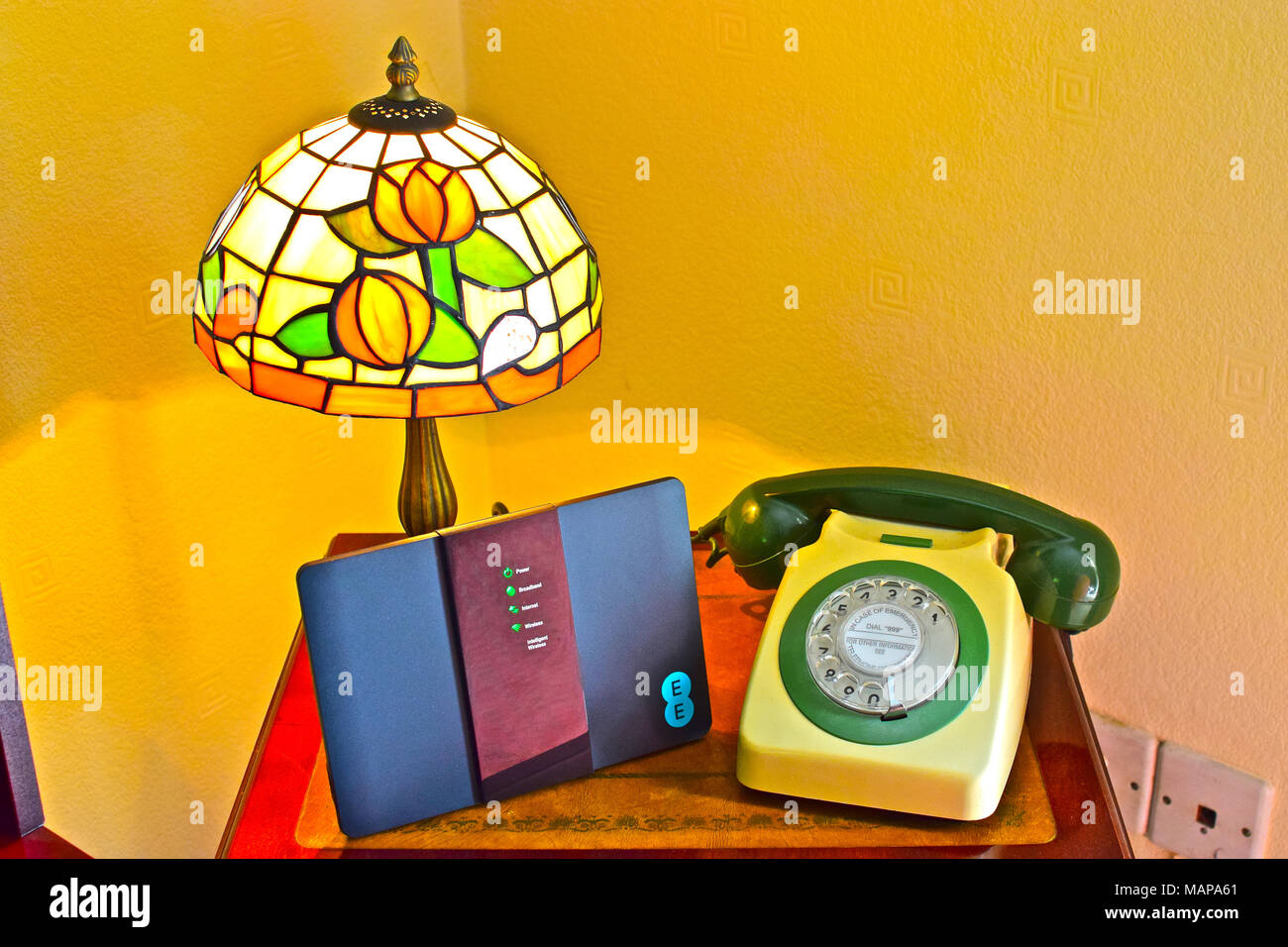 Comunicazioni vecchio e nuovo! Un telefono GPO risalente al 1972 (tipo 746F) si siede accanto a un moderno telecoms router, tutte sotto un retrò lampada Tiffany. Foto Stock