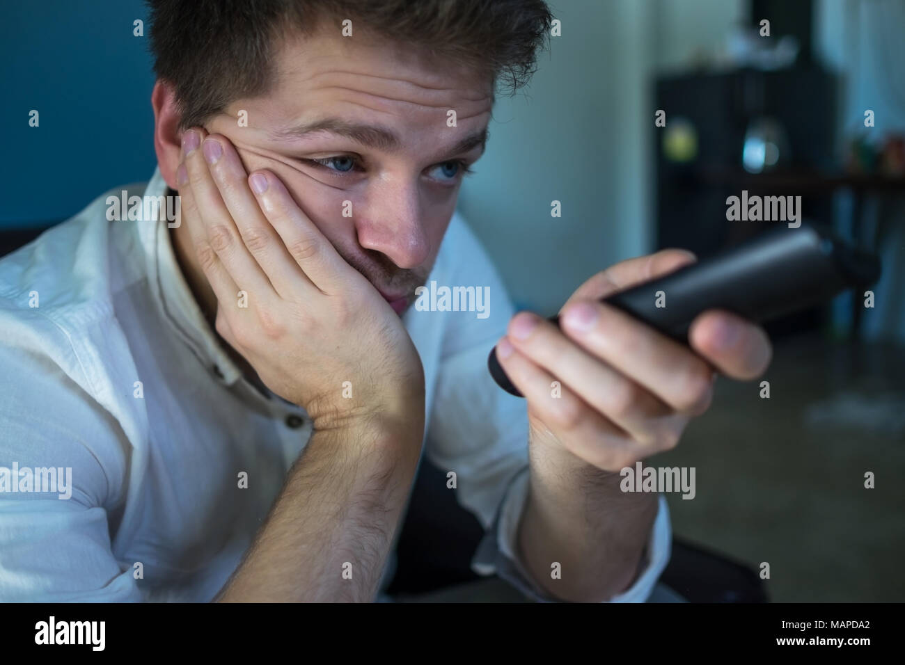 Annoiato uomo caucasico guardando la tv e lo zapping seduto su un divano a casa o in albergo. Foto Stock