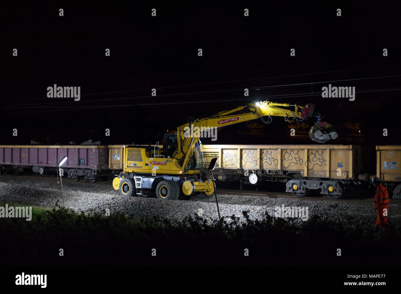 Stazione di lavoro di ingegneria di scavare fino via e caricarlo sul treno in attesa durante la notte la via di rinnovamento per la guida della rete sulla linea principale della costa occidentale Foto Stock