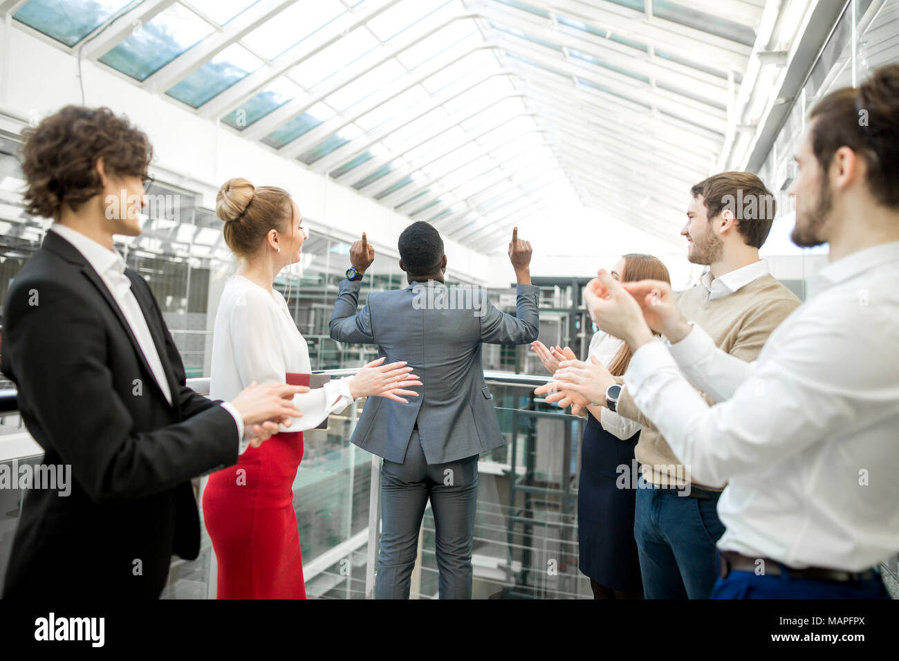 Due uomini di affari si stringono la mano mentre i loro colleghi applaudendo e sorridente Foto Stock