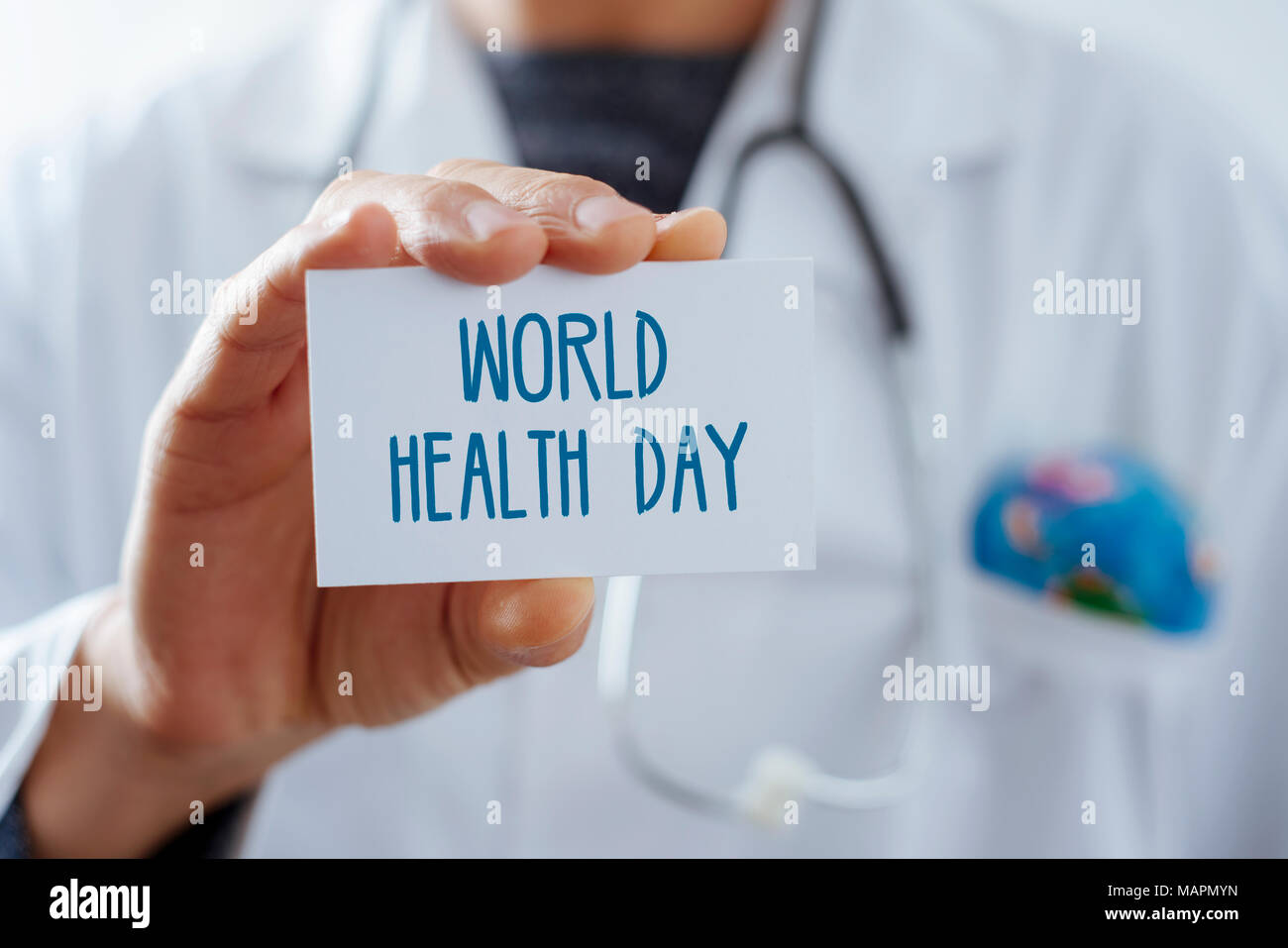 Primo piano di un giovane medico caucasica uomo, con un globo mondo nella tasca del suo mantello bianco, mostrando un cartello con scritto il testo giornata mondiale della salute writte Foto Stock