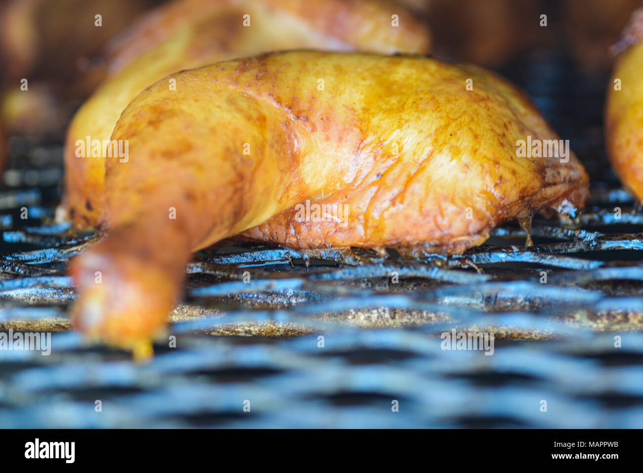 Fumato il pollo sul grill, close up di gamba e coscia con pelle dorata. Sfondo nero di smokehouse. Profondità di campo, il fuoco selettivo. Foto Stock