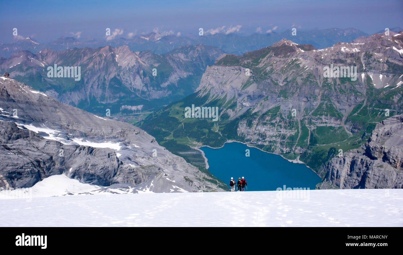 Guida di montagna con due client scende lungo un ripido ghiacciaio bianco con un fantastico blu del lago di montagna molto al di sotto di Foto Stock