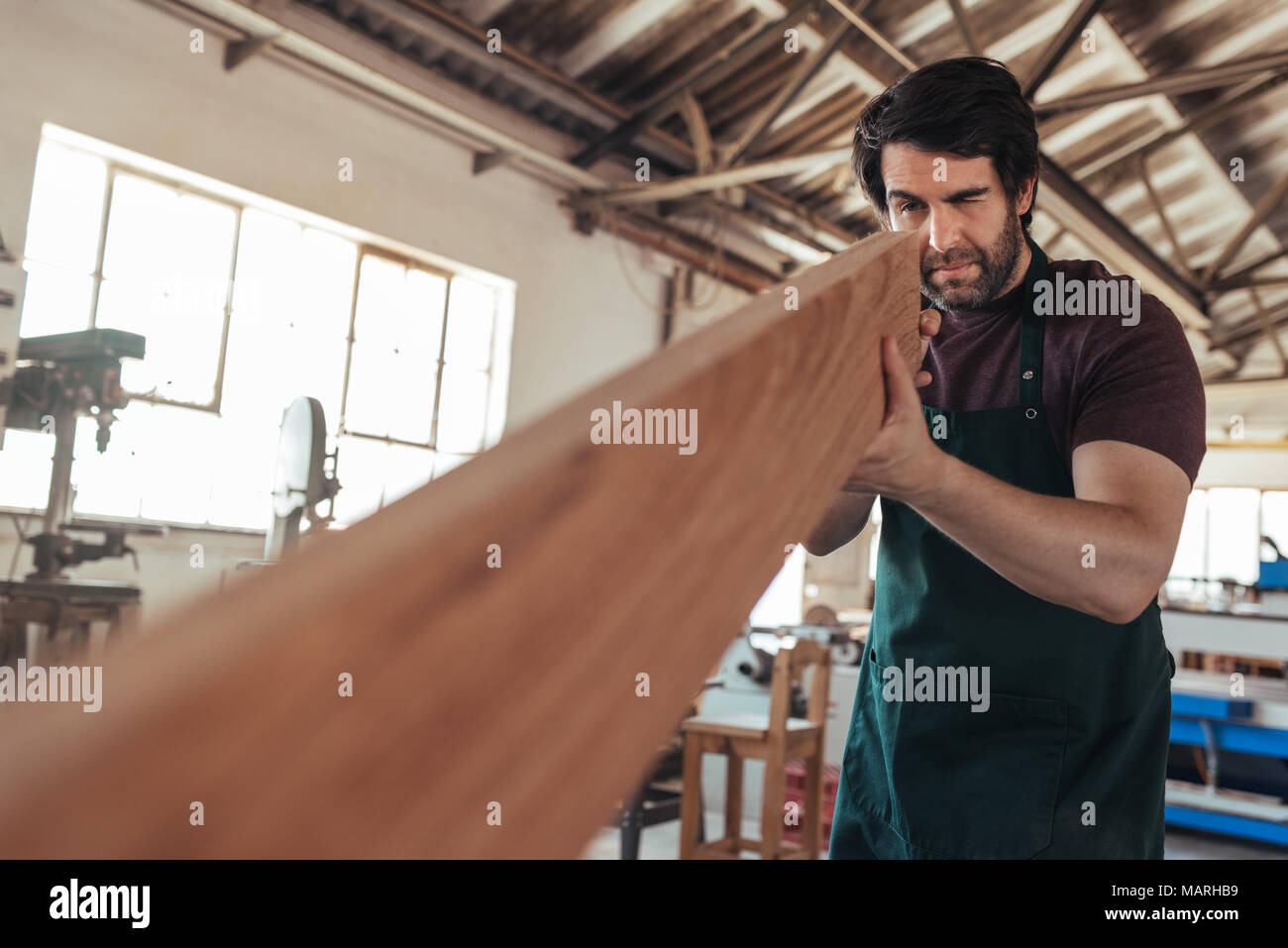 Artigiano esaminando un asse di legno nel suo laboratorio Foto Stock