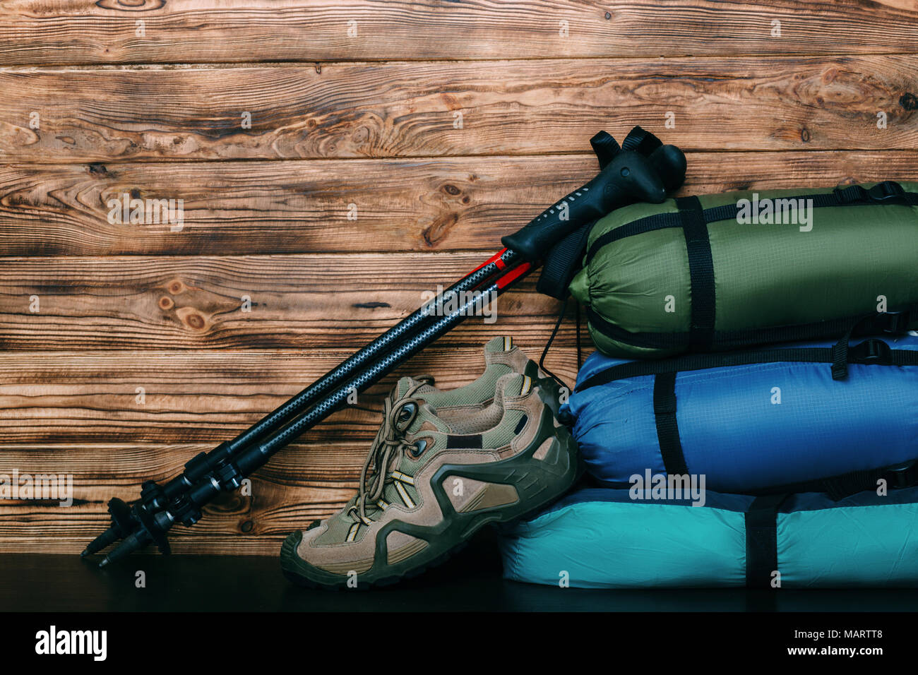 Stile di vita turistica con le scarpe da trekking, sacchi a pelo, tenda e pali trekking su sfondo di legno con copia spazio per il testo Foto Stock