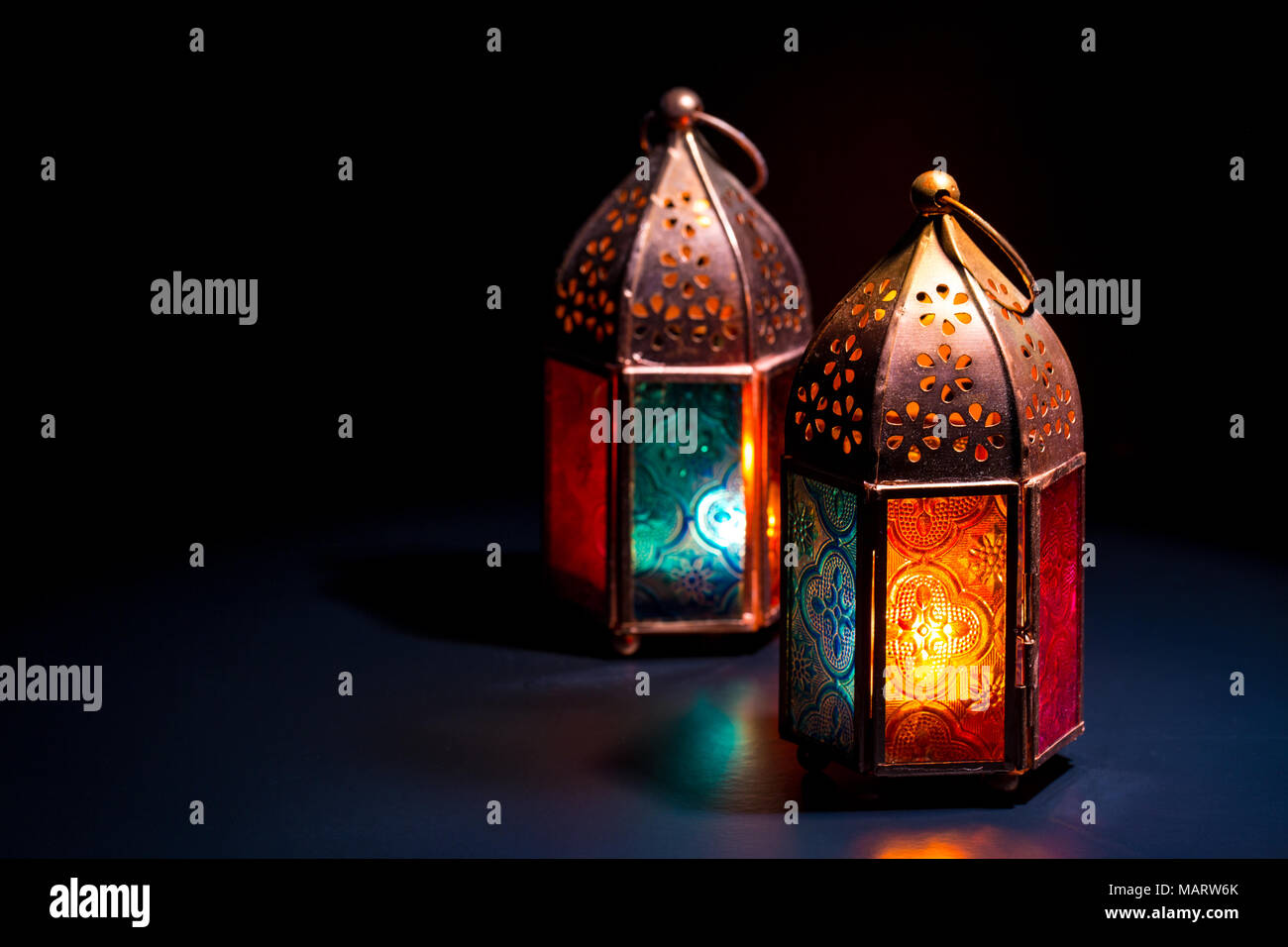 Due colorati lampada orientali lanterne masterizzare con candele con la riflessione di colore scuro su sfondo nero per il Ramadan e altri musulmani islamici vacanze, sp Foto Stock