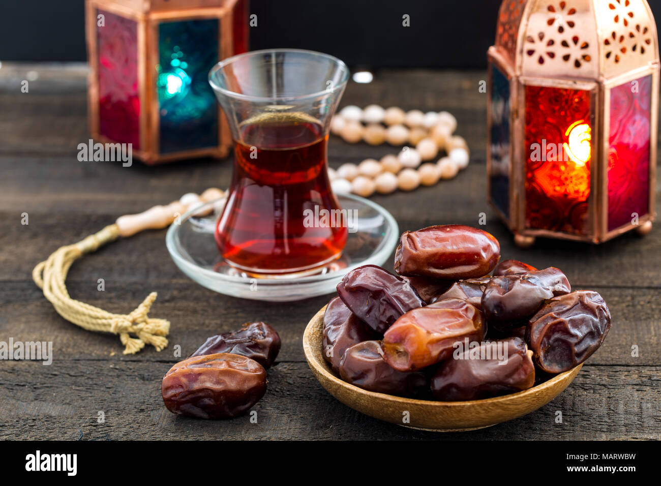 Il Ramadan Kareem festosa, close up date sul piatto di legno e il rosario con la lanterna orientale le lampade e la tazza di tè nero su uno sfondo di legno. Santa islamica Foto Stock