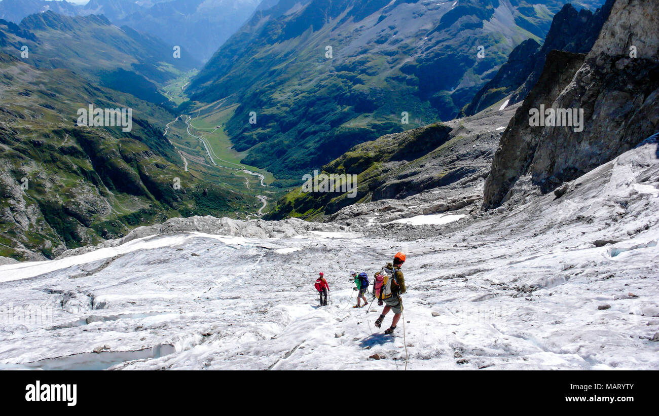 Gruppo dei maschi di alpinisti attraversando un ghiacciaio sulla loro strada verso il basso da un elevato picco alpino Foto Stock