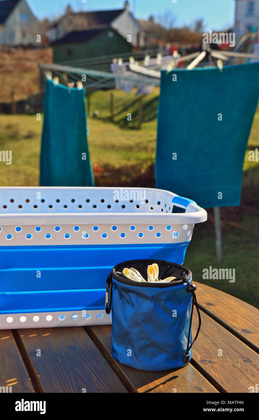 Cestello di lavaggio e vestiti peg cesto su una panchina da giardino con lavaggio al vento in background Foto Stock