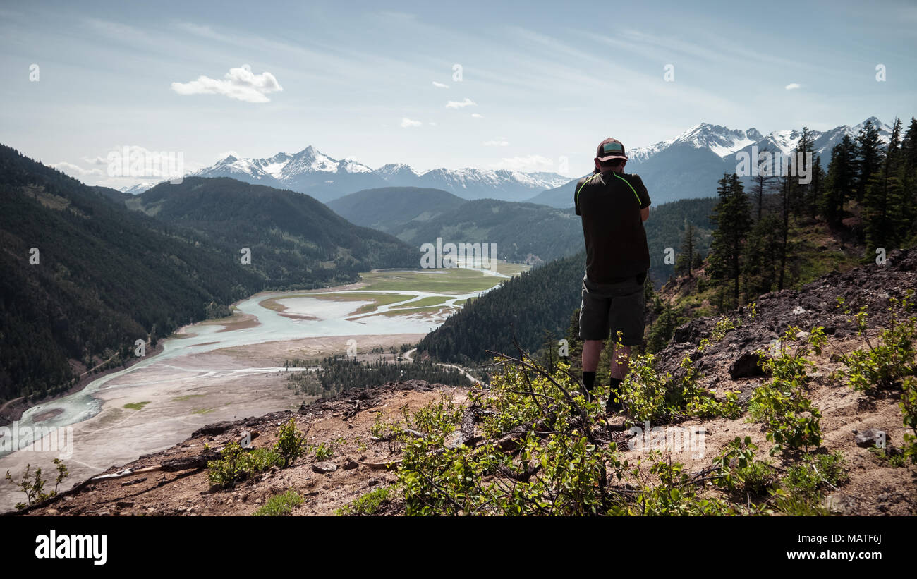 Un maschio di escursionista visualizzazione e photgraphing il ponte del fiume e Carpenter nel serbatoio il ponte sulla Valle del fiume da un belvedere (Gold Bridge, BC, Canada) Foto Stock