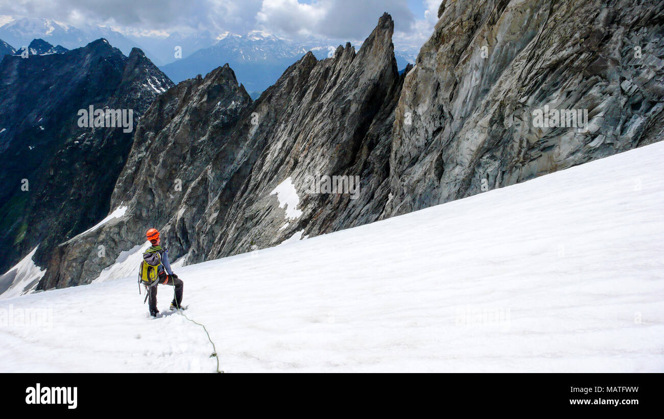 Maschio scalatore di montagna si prende una pausa su un alto ghiacciaio alpino e guarda la sua strada verso il basso e verso il percorso di discesa Foto Stock