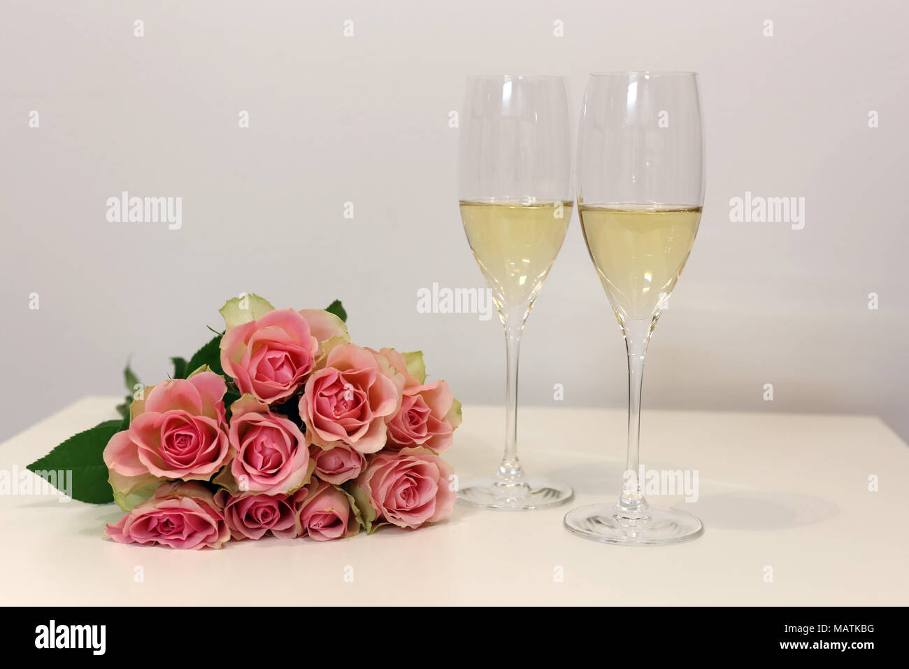 Due flauti champagne / spumante bicchieri fotografato su un tavolo bianco con un bouquet fatto di luce rosa rose. Celebrazione di lusso! Foto Stock