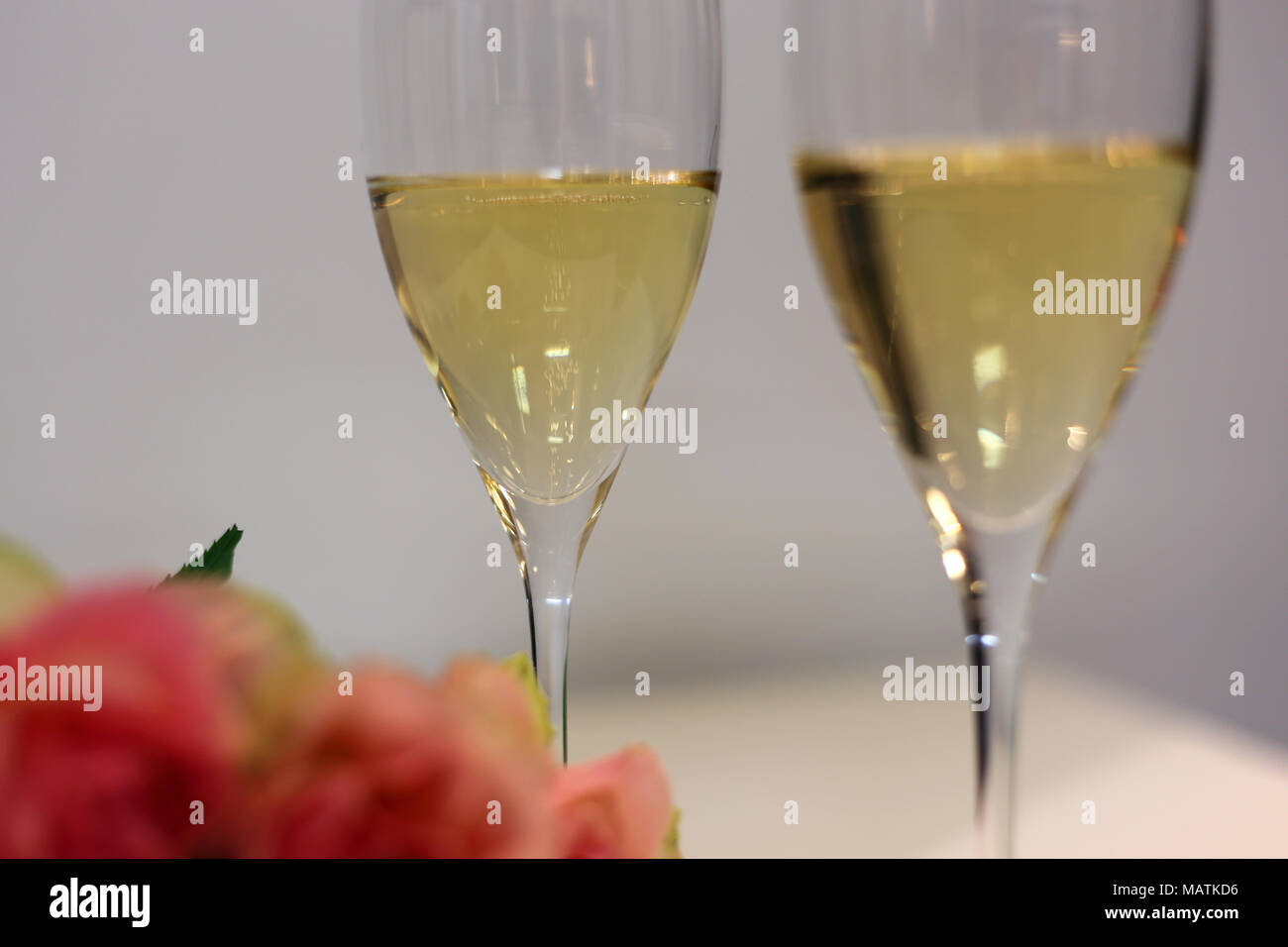Due flauti champagne / spumante bicchieri fotografato su un tavolo bianco con un bouquet fatto di luce rosa rose. Celebrazione di lusso! Foto Stock