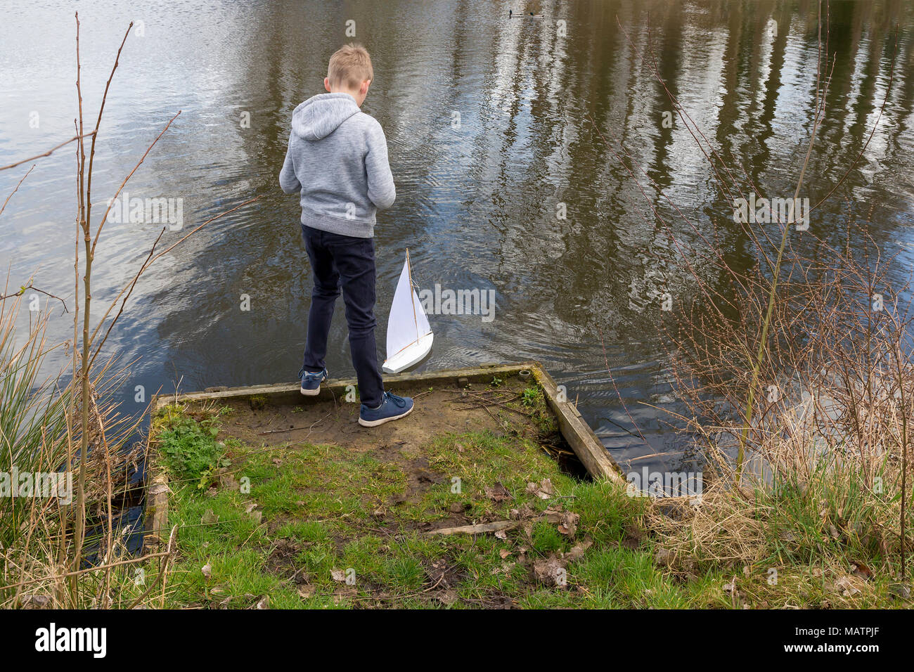 Un giovane ragazzo vele il suo yacht bianco sulle acque della fossa Ackers, Warrington, Cheshire, Inghilterra, Regno Unito il 03 aprile 2018 Foto Stock