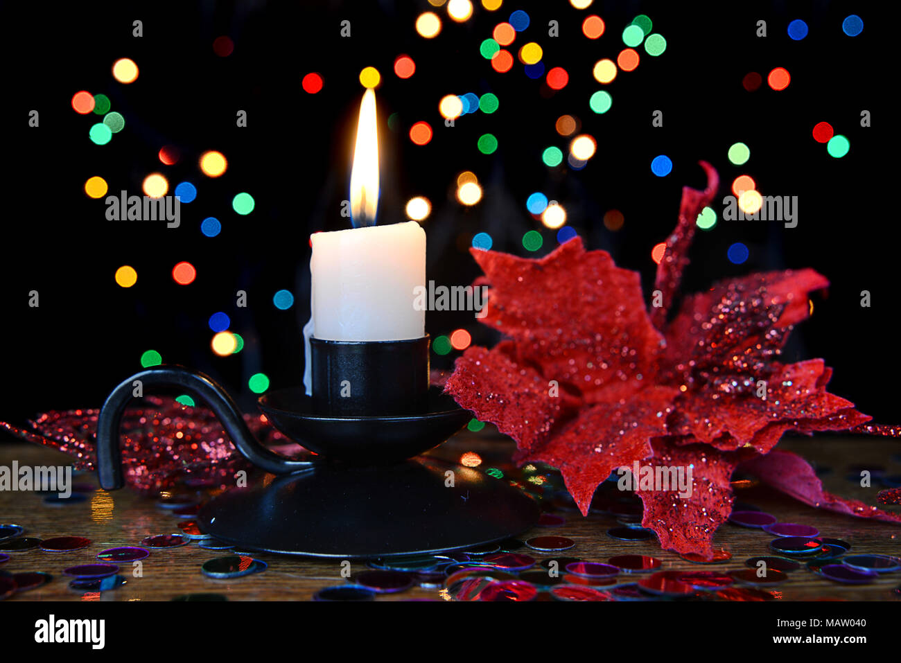 Candela che brucia in un candelabro nero e un fiore rosso contro un multicolore bokeh sfondo. Composizione di natale Foto Stock