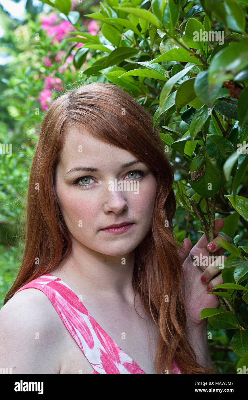 Una donna con i capelli rossi in piedi in un giardino. Foto Stock