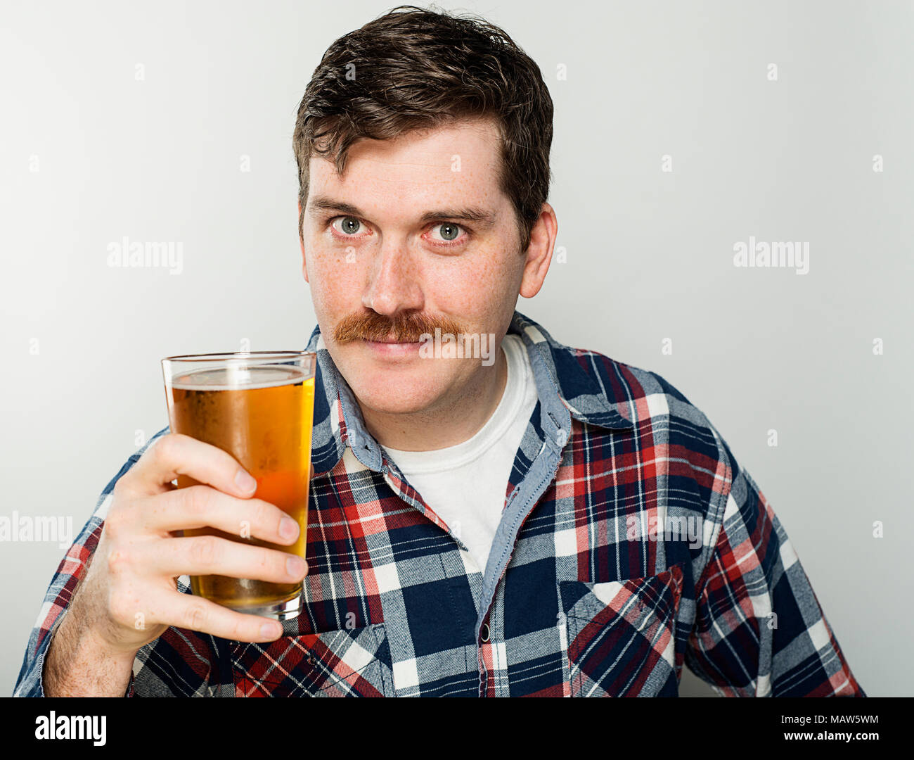 Un uomo con un baffi indossando un plaid shirt tenendo una birra. Foto Stock
