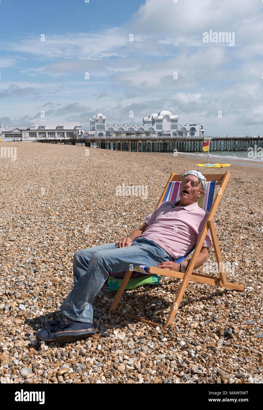 Uomo anziano che indossa un fazzoletto annodato sulla sua testa rilassante sulla spiaggia. Southsea, England Regno Unito Foto Stock