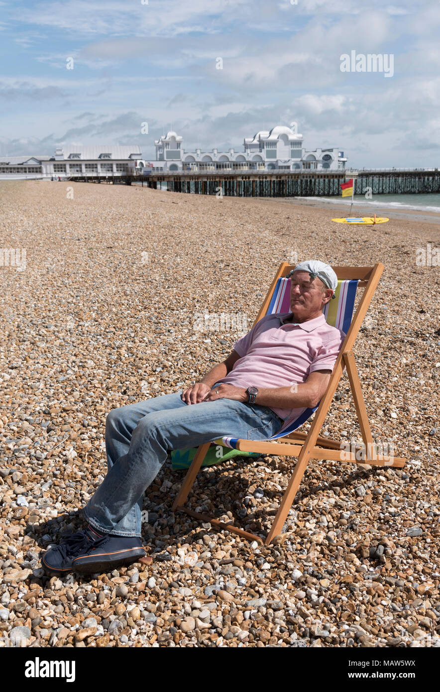 Uomo anziano che indossa un fazzoletto annodato sulla sua testa rilassante sulla spiaggia. Southsea, England Regno Unito Foto Stock