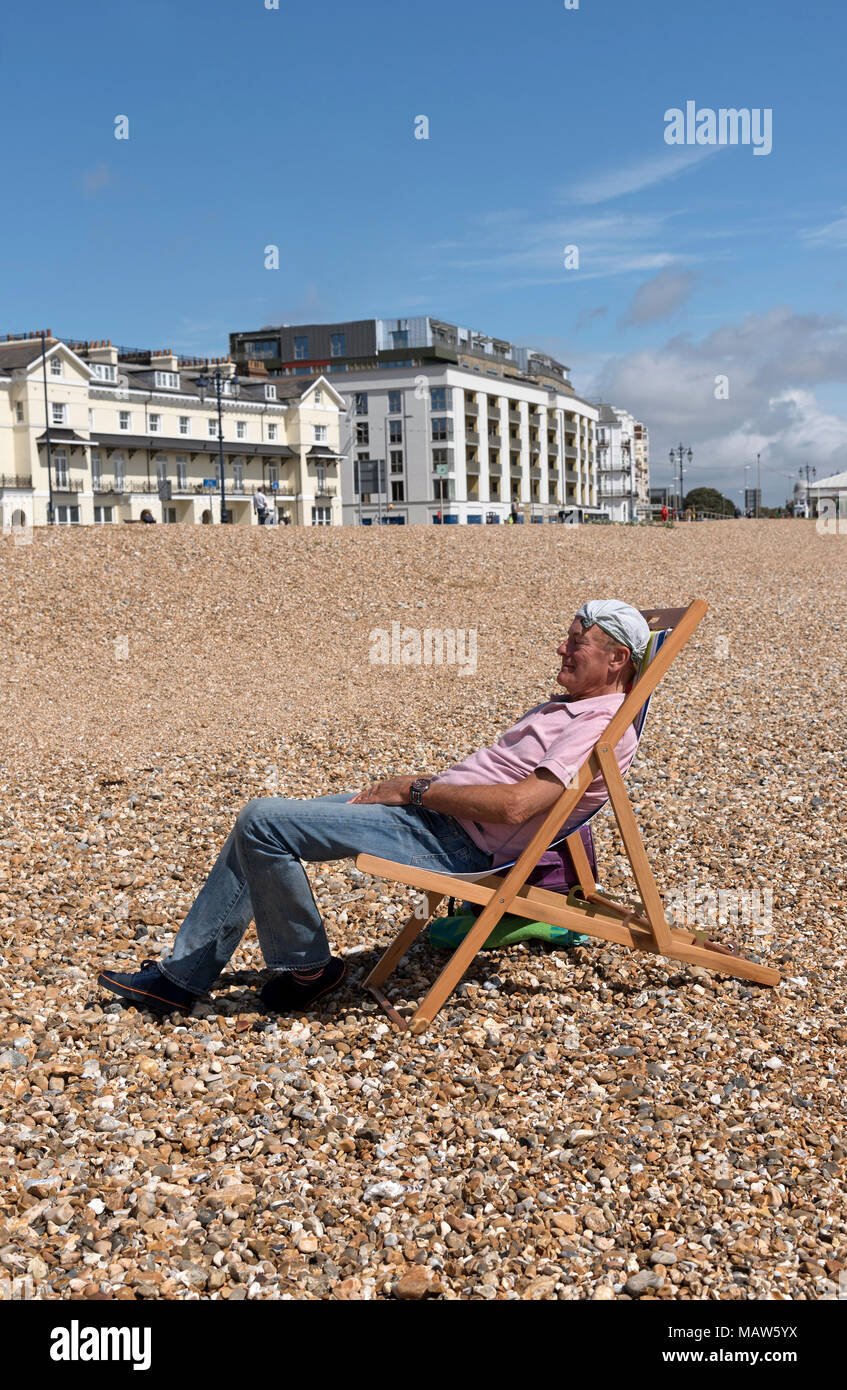 Uomo anziano che indossa un fazzoletto annodato sulla sua testa rilassante sulla spiaggia. Southsea, England Regno Unito Foto Stock