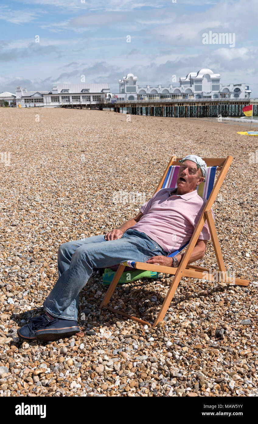Uomo anziano che indossa un fazzoletto annodato sulla sua testa rilassante sulla spiaggia. Southsea, England Regno Unito Foto Stock