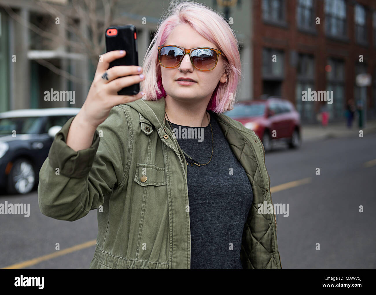 Una giovane donna con capelli rosa, in piedi in strada a Portland, Oregon con il suo telefono cellulare per scattare una foto. Foto Stock