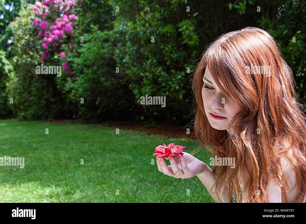 Una donna con i capelli rossi seduto in un giardino tenendo un fiore. Foto Stock